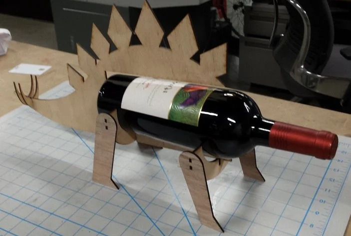 Prototype of a dinosaur-shaped wooden wine holder supporting a bottle