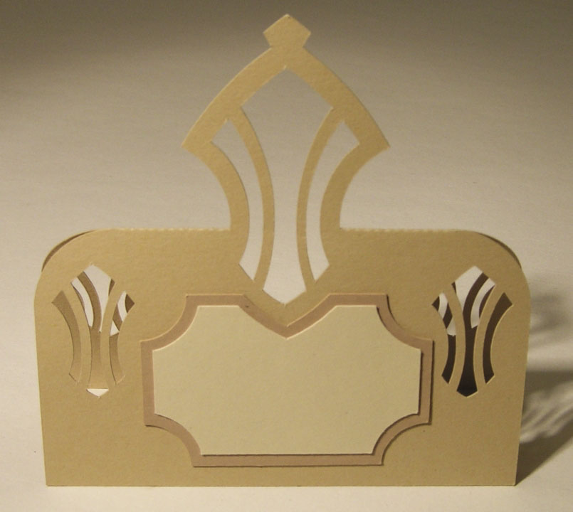 A gold-toned place card with a pointed openwork crest above a blank name panel